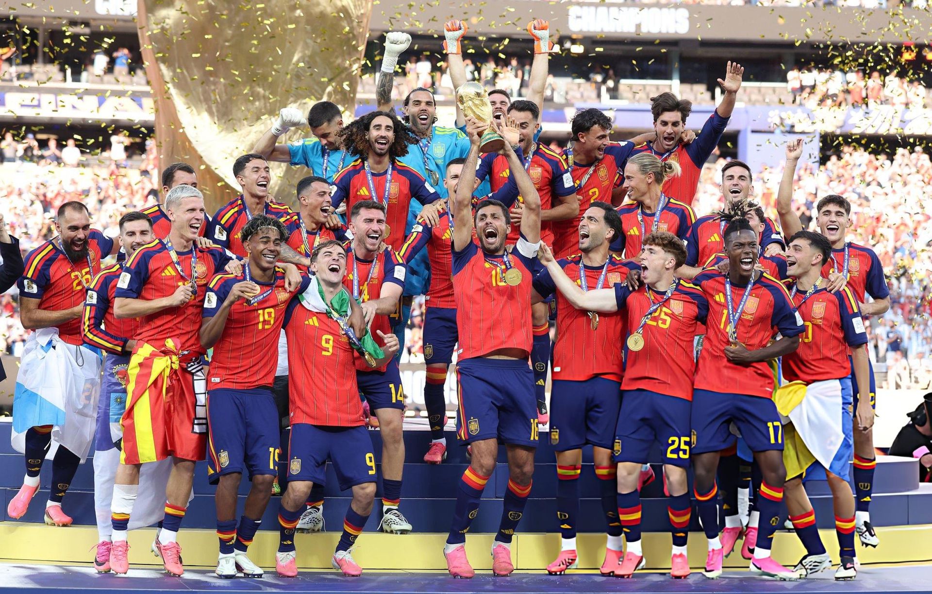 Spain players celebrate on the podium with the World Cup trophy and confetti falling